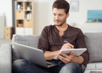 Mann mit Laptop macht sich auf einem Block Notizen