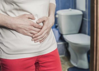 Ein Mann steht im Badezimmer vor der Toilette und fasst sich an den Bauch