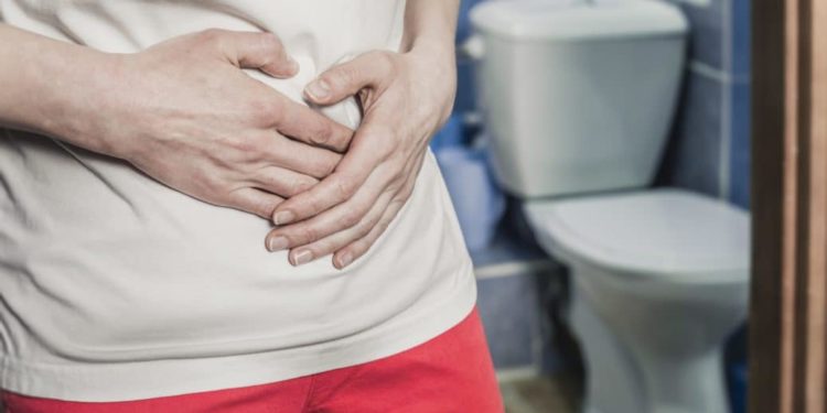 Ein Mann steht im Badezimmer vor der Toilette und fasst sich an den Bauch