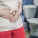 Ein Mann steht im Badezimmer vor der Toilette und fasst sich an den Bauch