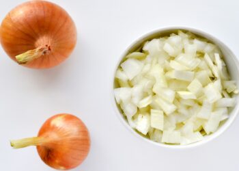 Zwei Zwiebeln neben einer Schale mit gehackten Zwiebel stückchen.