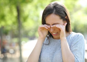Eine Frau steht in einem Park und reibt sich die Augen.