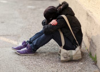 Junges Mädchen sitzt auf dem Boden und hat ihren Kopf in ihre verschränkten Arme gelegt