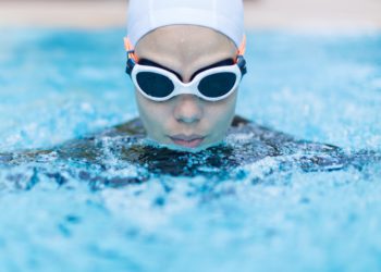 Eine Frau mit Schwimmbrille und Schwimmkappe beim Brustschwimmen.