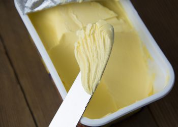 Margarine in einem Kunstoffbecher und ein Messer, mit welchem etwas davon entnommen wurde.