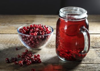 Preiselbeersaft in einem Glaskrug und frische Preiselbeeren auf dem Tisch