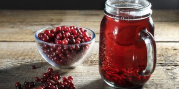 Preiselbeersaft in einem Glaskrug und frische Preiselbeeren auf dem Tisch