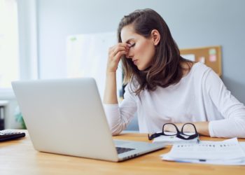 Gestresste junge Frau im Büro fasst sich mit einer Hand in das Gesicht