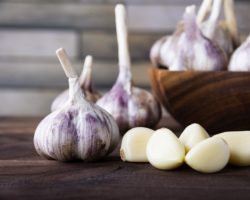 Knoblauchknollen und -zehen in und neben einer Holzschale.