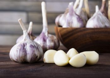 Knoblauchknollen und -zehen in und neben einer Holzschale.