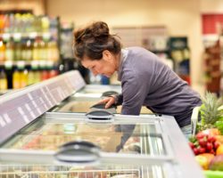 Frau holt Ware aus einer Tiefkühltheke im Supermarkt