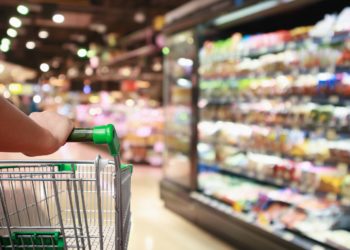 Eine Person schiebt einen Einkaufswagen durch einen Supermarkt.