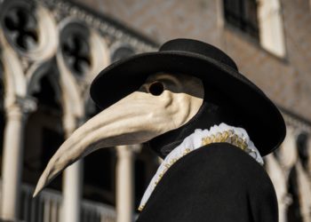 Eine als Pestdoktor mit Schnabelmaske und Hut verkleidete Person vor einem historischen Gebäude.