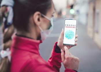 Eine Frau mit Mund-Nasen-Schutz schaut auf ihr Smartphone.