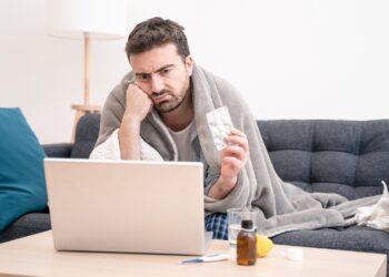 Ein kränklich aussehender Mann schaut auf einen Laptop.