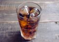 Ein mit Cola und Eiswürfeln gefülltes Glas auf einem Holztisch