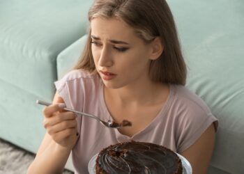 Eine Frau mit unglücklichem Gesichtsausdruck isst einen Schokoladenkuchen.