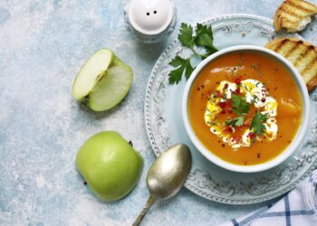 Eine Möhrensuppe wird auf einer weißen Oberfläche präsentiert.