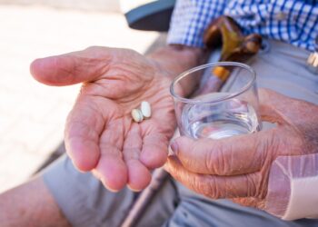 Senior mit zwei Tabletten und einem Glas Wasser in seinen Händen