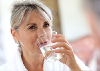 Eien Seniorin im Morgenmantel trinkt ein Glas Wasser