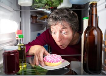 Eine Frau greift nach einem Donat im Kühlschrank.