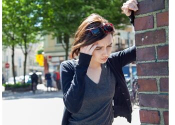 Eine Frau stützt sich an einer Wand ab und hält eine Hand an die Schläfe.