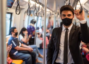 Junger Mann mit Anzug trägt in der U-Bahn eine Mund-Nasen-Bedeckung