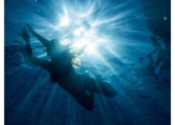 Ein Frau schwimmt bei strahlendem Sonnenschein im Wasser.