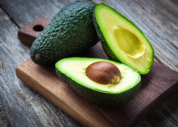 Eine ganze und eine aufgeschnittene Avocado auf einem Holzbrett