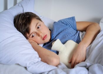 Ein Junge liegt mit einer Wärmflasche auf dem Bauch im Bett.