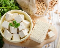 Tofu auf einem Holzbrett und in einer Schüssel neben einem Sack mit Sojabohnen