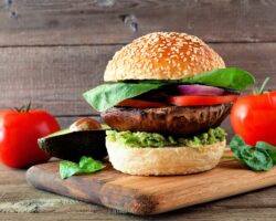 Veganer Burger mit Portobello-Pilz, Avocado, Tomate, Spinat und Zwiebeln auf einem hölzernen Servierbrett