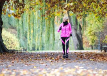 Eine Frau betreibt Nordic Walking in einer herbstlichen Landschaft.