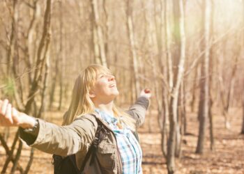 Frau genießt Sonnenstrahlen bei einer Wanderung im herbstlichen Wald