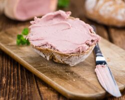 Brötchenhälfte bestrichen mit Leberwurst auf einem Brett neben einem Tafelmesser