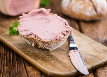 Brötchenhälfte bestrichen mit Leberwurst auf einem Brett neben einem Tafelmesser