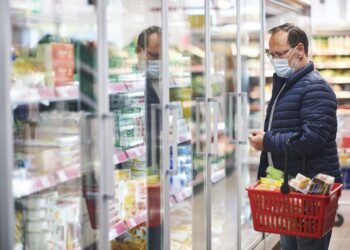 Mann mit Mund-Nasen-Bedeckung mit Einkaufskorb beim Einkaufen im Supermarkt