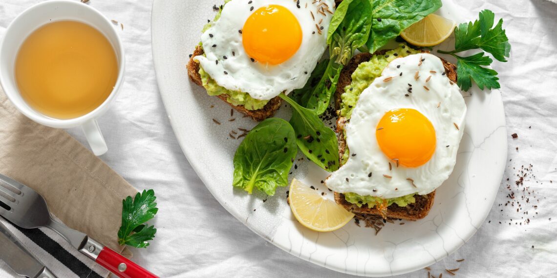 Gebratene Eier auf Brotscheiben mit Avocado neben einer Tasse Tee