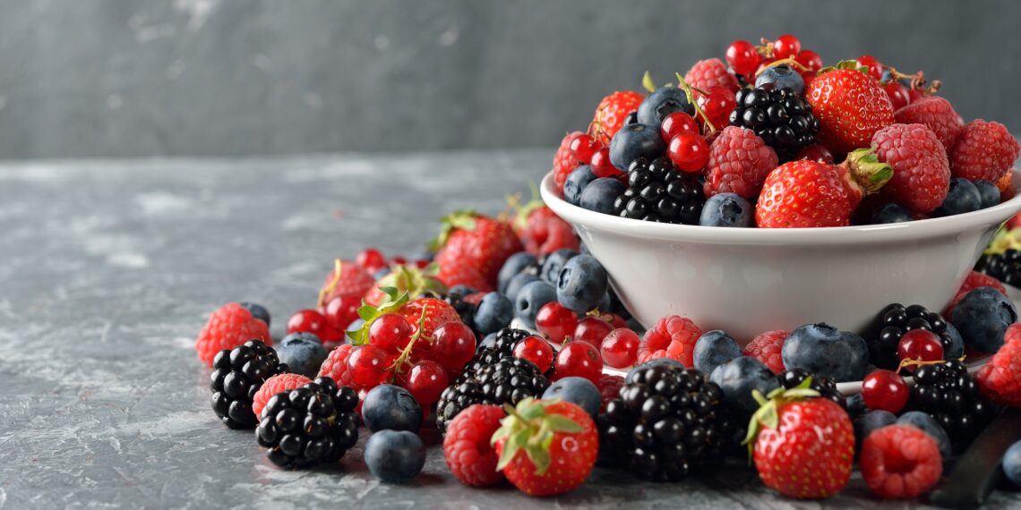 Verschiedene frische Beeren in einer Schüssel und auf einem Tisch