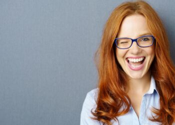 Rothaarige Frau mit Brille zwinkert mit einem Auge