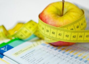 Ein Apfel und ein Maßband liegen neben einem Ernährungsplan.