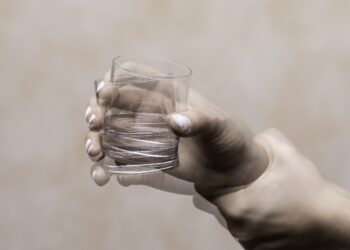 Eine zitternde Hand hält ein Glas mit Wasser fest.