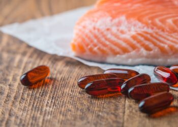 Omega-3-Pillen und ein Stück Lachs liegen auf einer hölzernen Oberfläche.