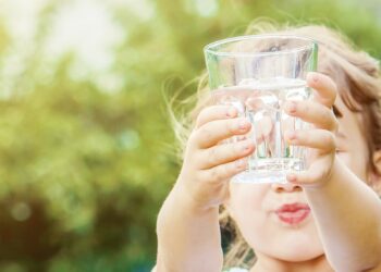 Mädchen hält mit beiden Händen ein Wasserglas nach oben