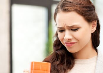 Eine Frau mit einer Kaffeetasse in der Hand verzieht das Gesicht.