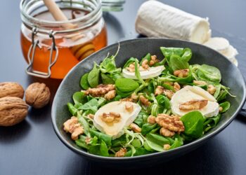 Teller mit Feldsalat mit Ziegenkäse und Walnüssen neben einem Glas Honig und einer Ziegenkäserolle