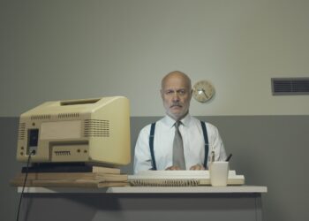 Ein ordentlich gekleideter Mann sitzt an einem Schreibtisch in einem Büro.