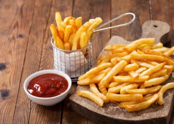 Eine Portion Pommes frites ist auf einem Holzbrett angerichtet.