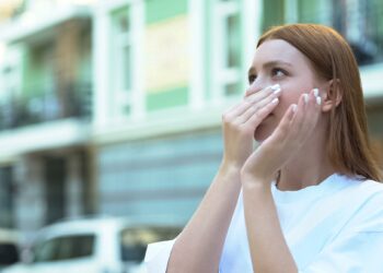 Eine Frau steht auf der Straße und hält sich die Nase zu.