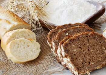 Ein Weißbrot und einige Scheiben Vollkornbrot liegen auf einer hölzernen Oberfläche.